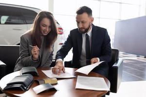 young woman buys a new car in a car dealership and signs documents, car insurance concept photo
