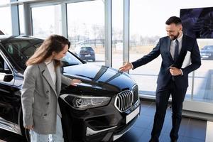 una mujer joven en un concesionario de automóviles elige un automóvil nuevo junto con un gerente, concepto de alquiler de automóviles foto