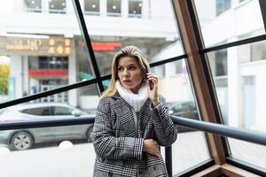 Business woman blonde talking on a mobile phone against the background of the glass facade of the building photo