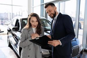 mujer joven versada en el poste de seguros de automóviles junto con un consultor en un concesionario de automóviles foto