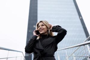 mujer de negocios hablando por un teléfono móvil alisando su cabello en el fondo de un edificio de oficinas de varios pisos foto