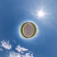 tiny planet in blue overcast sky with beautiful clouds with transformation of spherical panorama 360 degrees. Spherical abstract aerial view. Curvature of space. photo