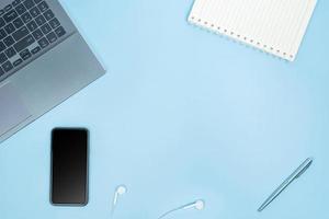 Top view of Office Table top with laptop computer, notebook, smart phone, pen, head phones on blue table with space photo