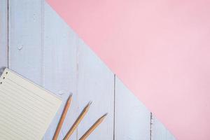 Top view image of notebook with pencils on wooden table with pink background photo