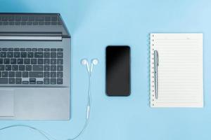 Top view of Office Table top with laptop computer, notebook, smart phone, pen, head phones on blue table photo