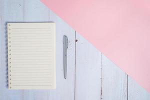 Top view image of notebook with pen on wooden table with pink background photo