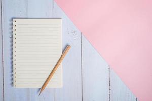 Top view image of notebook with pencil on wooden table with pink background photo