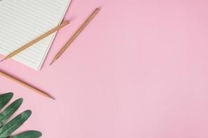 Top view image of notebook with pencils and xanadu leaf on pink background photo