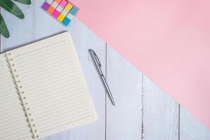 Top view image of notebook with pen and xanadu leaf on wooden table with pink background photo