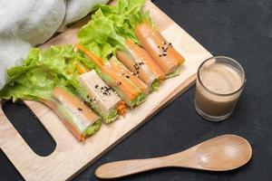 Salad roll on wooden tray with salad dressing and wooden spoon and cloth linen on wooden black table. photo