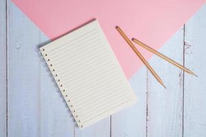 Top view image of notebook with pencils on wooden table with pink background photo