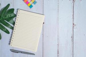 Top view image of notebook with pen and xanadu leaf on wooden table photo