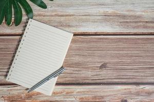 Top view image of notebook with pen and xanadu leaf on wooden table photo