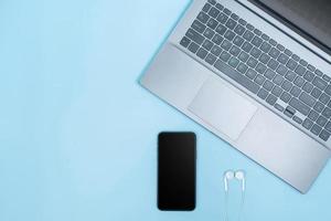 Top view of Office Table top with laptop computer,  smart phone, head phones on blue table with space photo