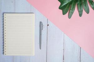 Top view image of notebook with pen and xanadu leaf on wooden table with pink background photo