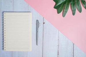 imagen de la vista superior del cuaderno con bolígrafo y hoja de xanadu sobre una mesa de madera con fondo rosa foto