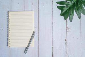 Top view image of notebook with pen and xanadu leaf on wooden table photo