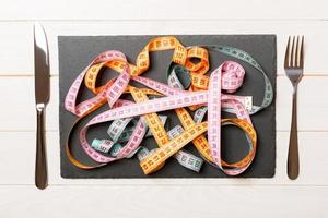 Top view of heap of colorful measuring tapes in plate on wooden background. Diet concept with copy space photo