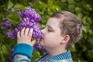 The boy sniffs a lush branch of lilac. Close-up portrait. Natural wallpaper. Selective focus. photo