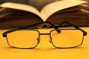 Glasses in a black frame on a yellow background. In the background is an open book. World Day of Sight. photo