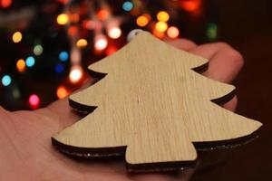 árbol de navidad hecho de madera hecha a mano en una mano femenina contra el fondo de una guirnalda de navidad. concepto de navidad, año nuevo, ecología. foto