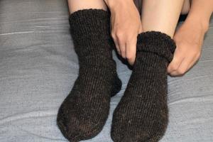 A young woman with slender legs sits on the bed at home and puts on woolen socks. The concept of the world energy crisis. photo