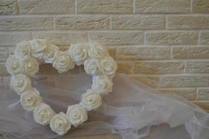White heart with white roses and diamonds. Background of beige bricks. White transparent fabric. photo