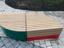 a wooden bench in the center of the residential complex in the form of a droplet. seating area with red and green color. wooden seat for shoppers and visitors of the mall. wooden boards on the benches photo