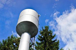 gran torre de agua industrial de acero inoxidable brillante para suministrar agua de gran capacidad, barril contra el cielo azul y los árboles foto