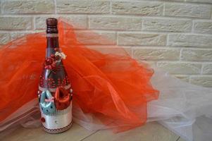 A homemade bottle of champagne decorated with toy hares and flowers against a background of red and white fabric and a brick wall. photo