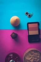 Beauty box, makeup kit, powder and blush with beauty blender, perfume, lipstick, highlighter and earrings for makeup on a pink purple and blue background. Flat lay. Top view photo