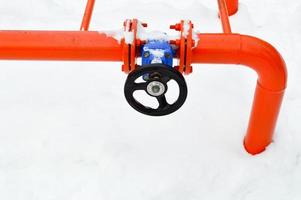 Industrial shut-off regulating protective pipe fittings. Black valve for opening, closing on an iron orange metal pipe with flanges, studs, nuts against the background of white snow in winter photo