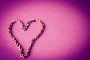 Texture of a beautiful golden festive chain unique weaving in the shape of a heart on a pink purple background and copy space. Concept love, marriage proposal, marriage, St. Valentine's Day photo