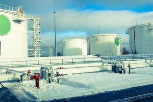 grandes tanques industriales de metal de hierro blanco para almacenamiento de combustible, gasolina y diesel y tuberías con válvulas y bridas en la refinería en invierno foto