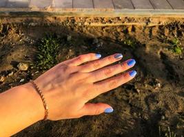hand with blue manicure on sand background. a new color of nails for a girl with a gold bracelet. in the background - the construction of a new area, dirt and building materials. photo