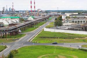 Industrial landscape. Panoramic view of the technological pipes. Plant settings. From the chemical red-white pipes smoke is coming. Production buildings. Against background of sky and bright grass photo