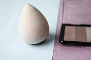 Beauty box, a set of women's cosmetics, crumbly matte mineral powder and blush with a beauty blender for makeup on a pink purple and blue background. Flat lay. Top view photo