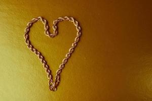 Texture of a beautiful golden festive chain unique weaving in the shape of a heart on a yellow gold background and copy space. Concept love, marriage proposal, marriage, St. Valentine's Day photo