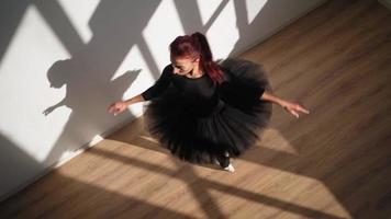 skön ballerina i en svart tutu och pointe skor graciöst danser mot en vit vägg i ljus solljus. långsam rörelse. topp se video