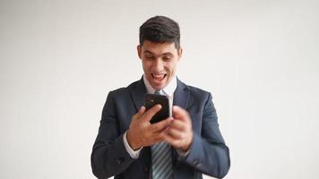 Happy male office worker in formal clothes uses mobile phone and rejoices in victory on white background. Businessman in jacket and tie experiences triumph of the winner, laughs with joy. video