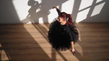 bellissimo ballerina nel un' nero tutu e pointe scarpe con grazia balli contro un' bianca parete nel luminosa luce del sole. lento movimento. superiore Visualizza video