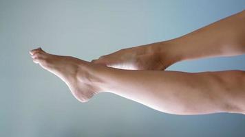 video vertikal, hermosas piernas femeninas desnudas bien cuidadas con piel limpia se mueven con gracia sobre un fondo gris. concepto de cuidado de pies y cuerpo. belleza y salud de los pies