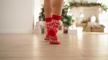 avvicinamento, bellissimo femmina gambe nel rosso nuovo anni calzini siamo adatto per decorazione un' Natale albero su in punta di piedi. nuovo anno, inverno atmosfera, caldo luce. festivo umore. video