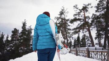 meisje in een ski pak wandelingen met een snowboard in haar handen in de sneeuw. winter buitenshuis activiteiten. gratis rit. langzaam beweging. video