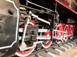 grandes ruedas de hierro de un tren rojo y negro parado sobre rieles y elementos de suspensión con resortes de una vieja locomotora de vapor industrial foto