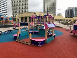 parque infantil rosa en el centro del conjunto residencial. para los niños hay columpios, ábacos, divertidos toboganes y estructuras para trepar. parque infantil junto al centro comercial y altas casas blancas foto