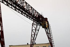 grúa de pórtico de metal grande de hierro industrial con un gancho montado en los soportes para levantar y transportar carga pesada, moviéndose a lo largo de los rieles en la fábrica. la grúa es de tipo puente foto