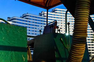 un camión para colocar asfalto se alza contra el fondo de una casa azul y blanca. asiento del conductor, caja de cambios y asiento verde. máquina verde con un tubo volumétrico amarillo foto