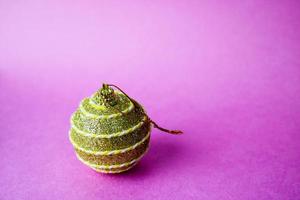 Golden yellow small round glass plastic winter smart shiny decorative beautiful xmas festive Christmas ball, Christmas toy pasted over with spangles on a violet pink background photo