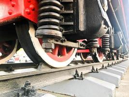 grandes ruedas de hierro de un tren rojo y negro parado sobre rieles y elementos de suspensión con resortes de una vieja locomotora de vapor industrial foto